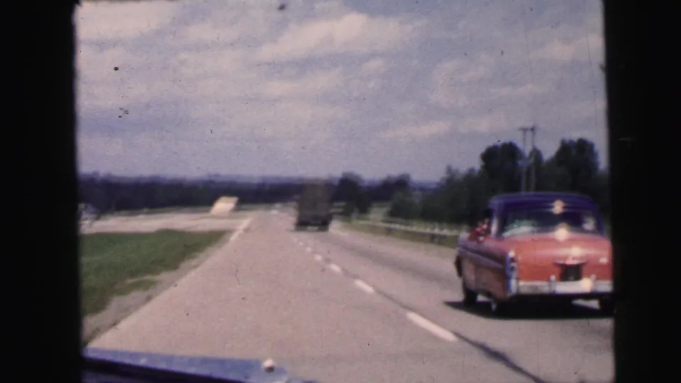 The closing frame keeps the moving highway view, with the pink sedan at right and a truck ahead under a mottled sky.