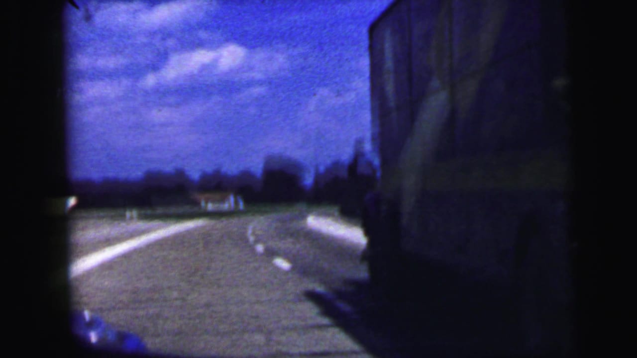 Highway curve and roadside shoulder framed by a dark car interior.