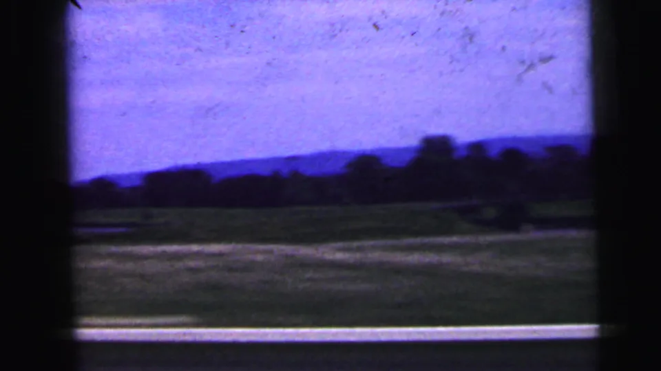1964 rural New Jersey road-trip frame with open fields, a low horizon, and trees viewed through a moving vehicle window.
