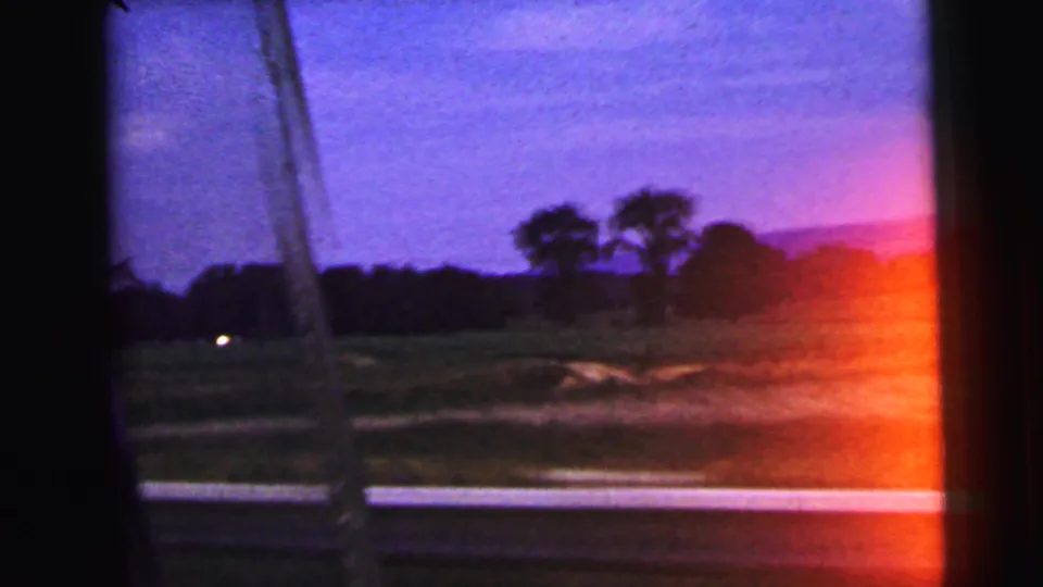 1964 rural New Jersey passenger-window view with fields, trees, a roadside edge, and an orange light leak on the film.