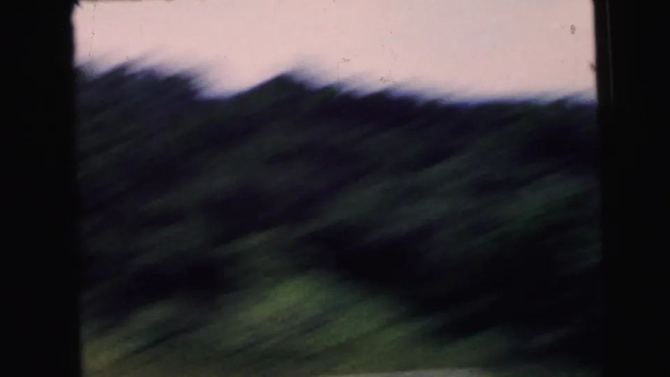 A moving 8mm car-window view in Camden, New Jersey, with blurred roadside greenery and dark vertical window frames.
