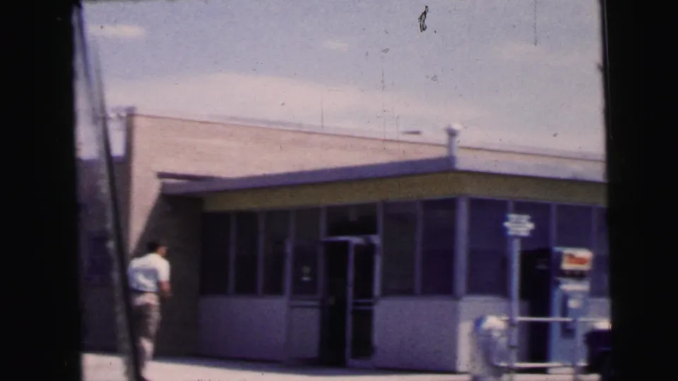 A man in light clothing walks near a low, glass-front roadside gas station building in the Camden, New Jersey home movie.