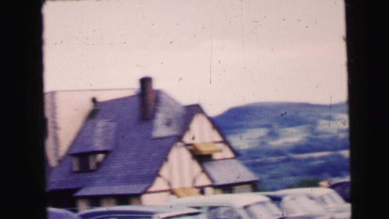 Gabled building roof with parked cars and rolling hills in the background.