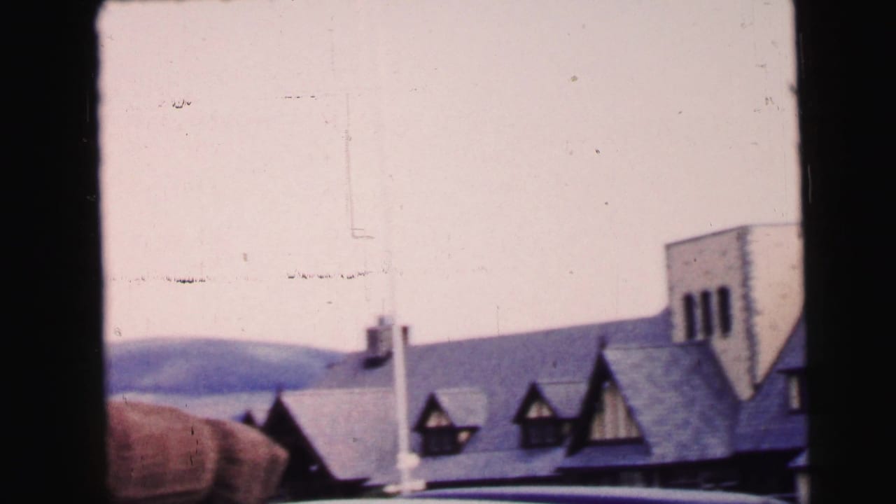Large gabled building with dormer windows and hills behind it.