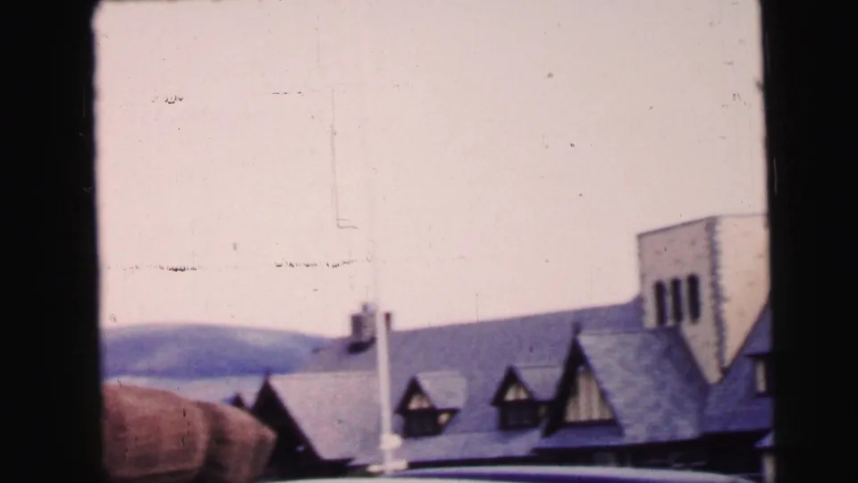 1964 Camden, New Jersey frame with dormer windows, a broad roofline, a pale sky, and low hills behind the building.