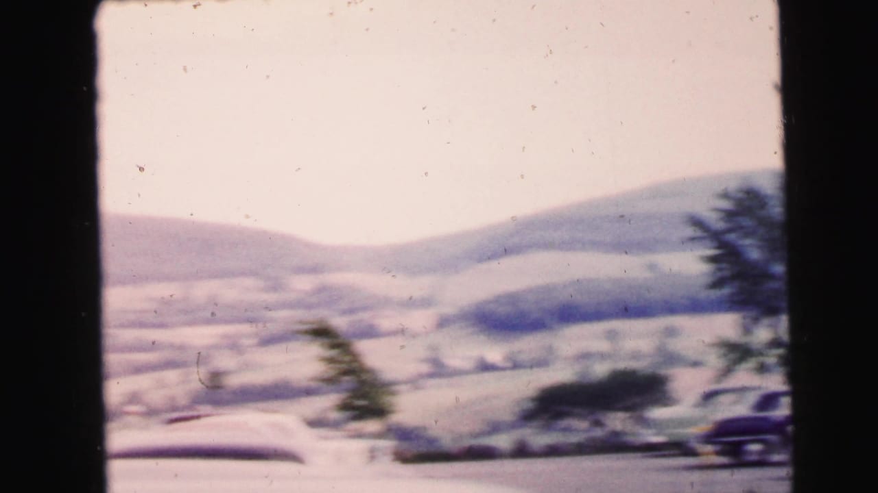 Parked cars seen through a dark frame with rolling hills in the background.
