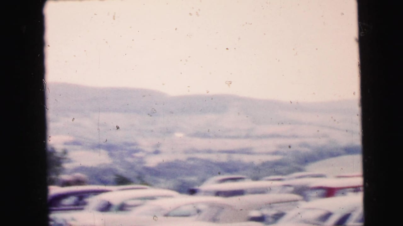 Rows of mid-century parked cars appear below rolling hills in this 1964 Camden-area home-movie frame.
