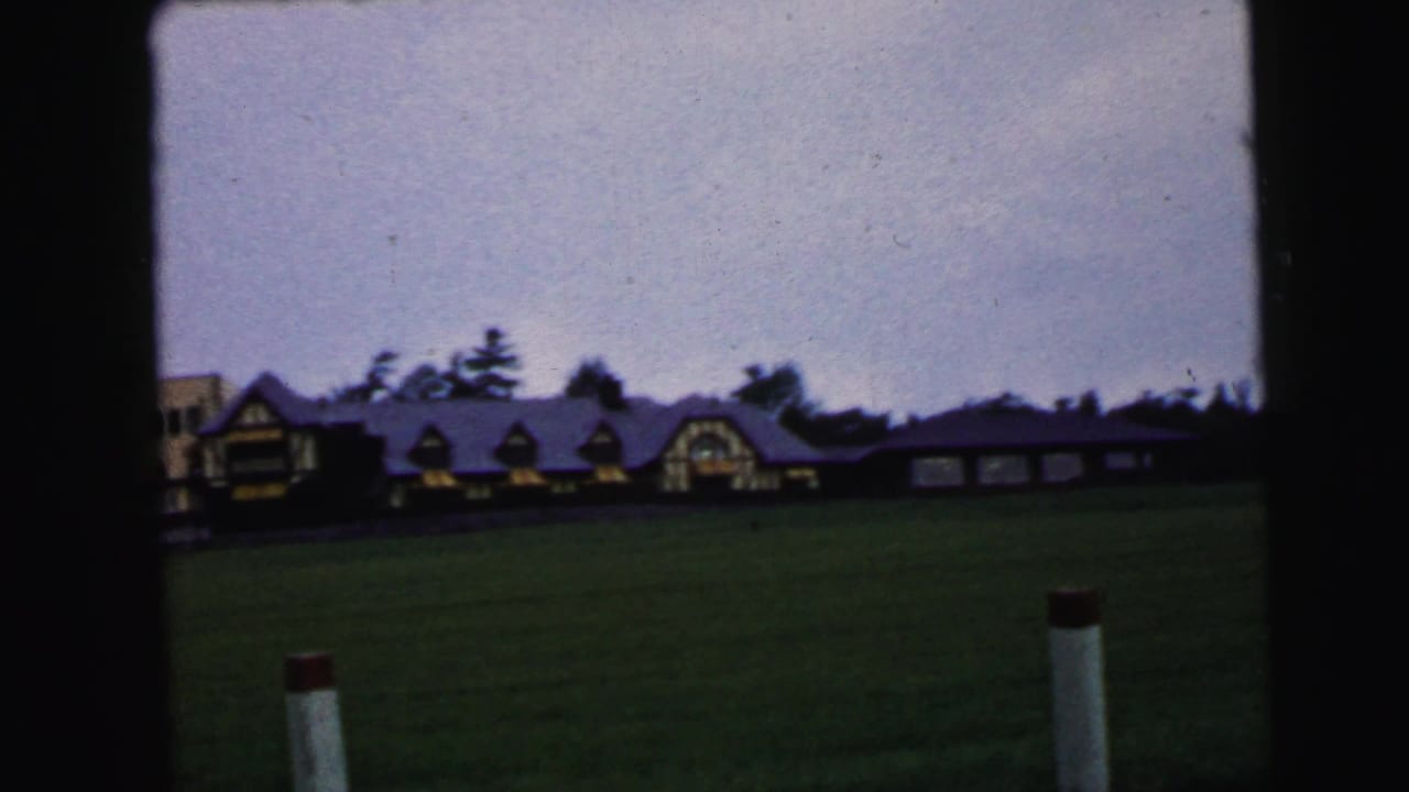 Camden-area 1964 exterior view of a long, low building and open grass as storm clouds move overhead.