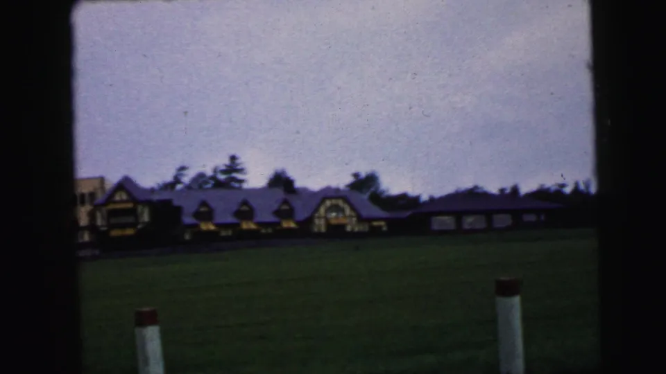 Camden-area 1964 exterior view of a long, low building and open grass as storm clouds move overhead.