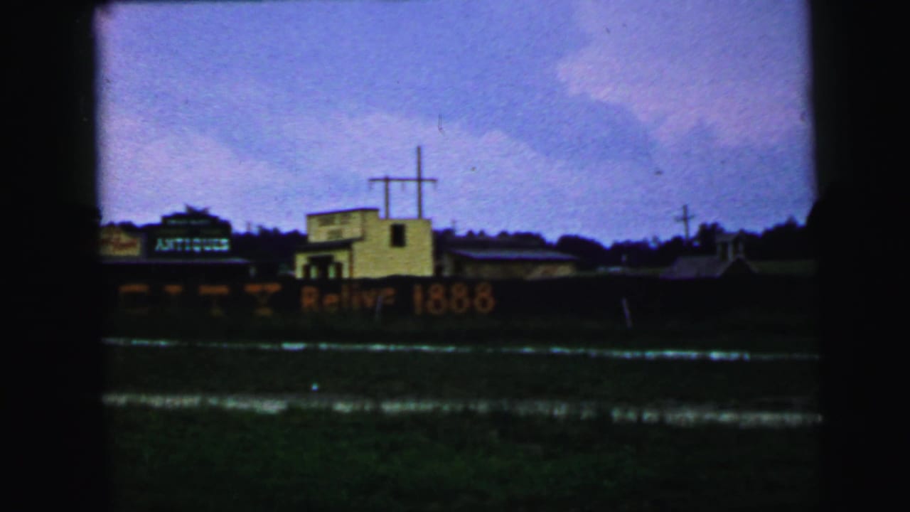 1964 Camden, New Jersey frame with a rail car marked Antiques and Relive 1888, a yellow building with a cross, utility poles, and trees.