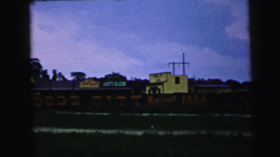 1964 Camden, New Jersey home-movie frame centered on the antiques rail car display and nearby yellow building with a prominent cross.