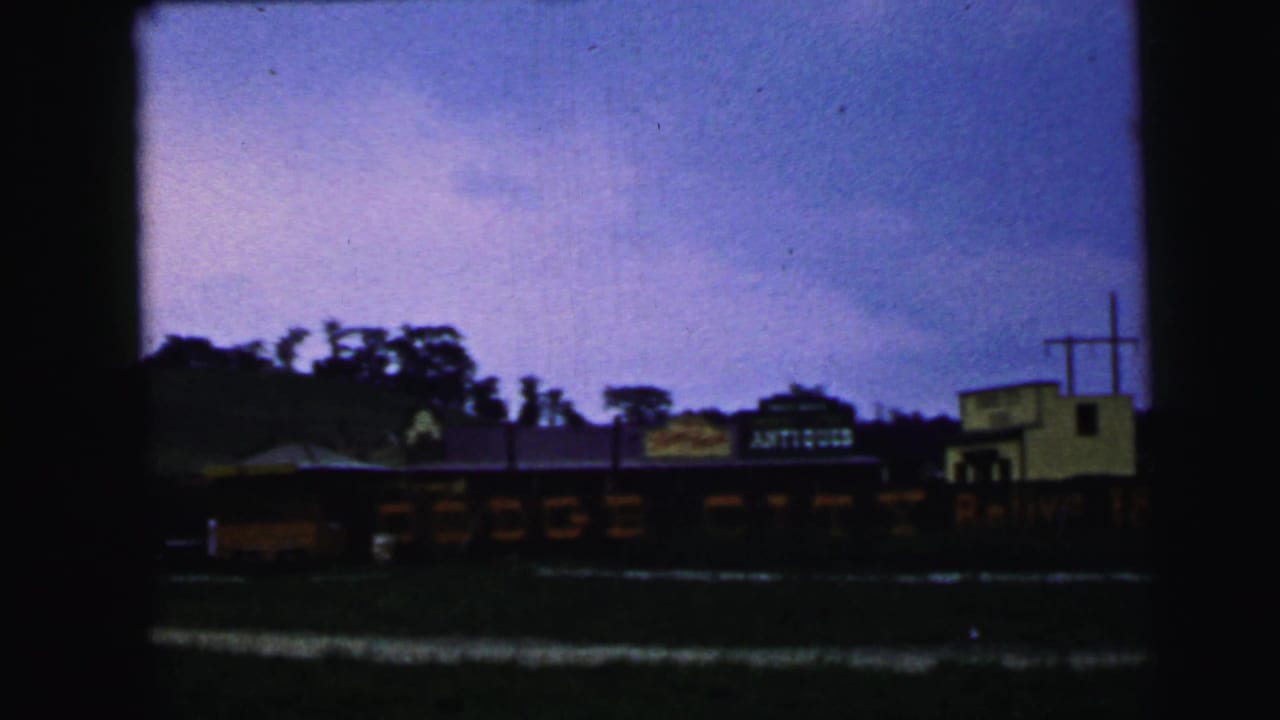 Roadside buildings beneath a purple sky, including a yellow structure and an antiques sign.