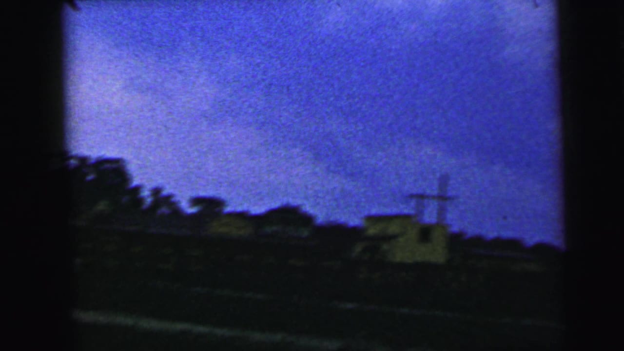 Dark rural horizon with trees, a small pale structure, utility pole, and blue dusk sky.