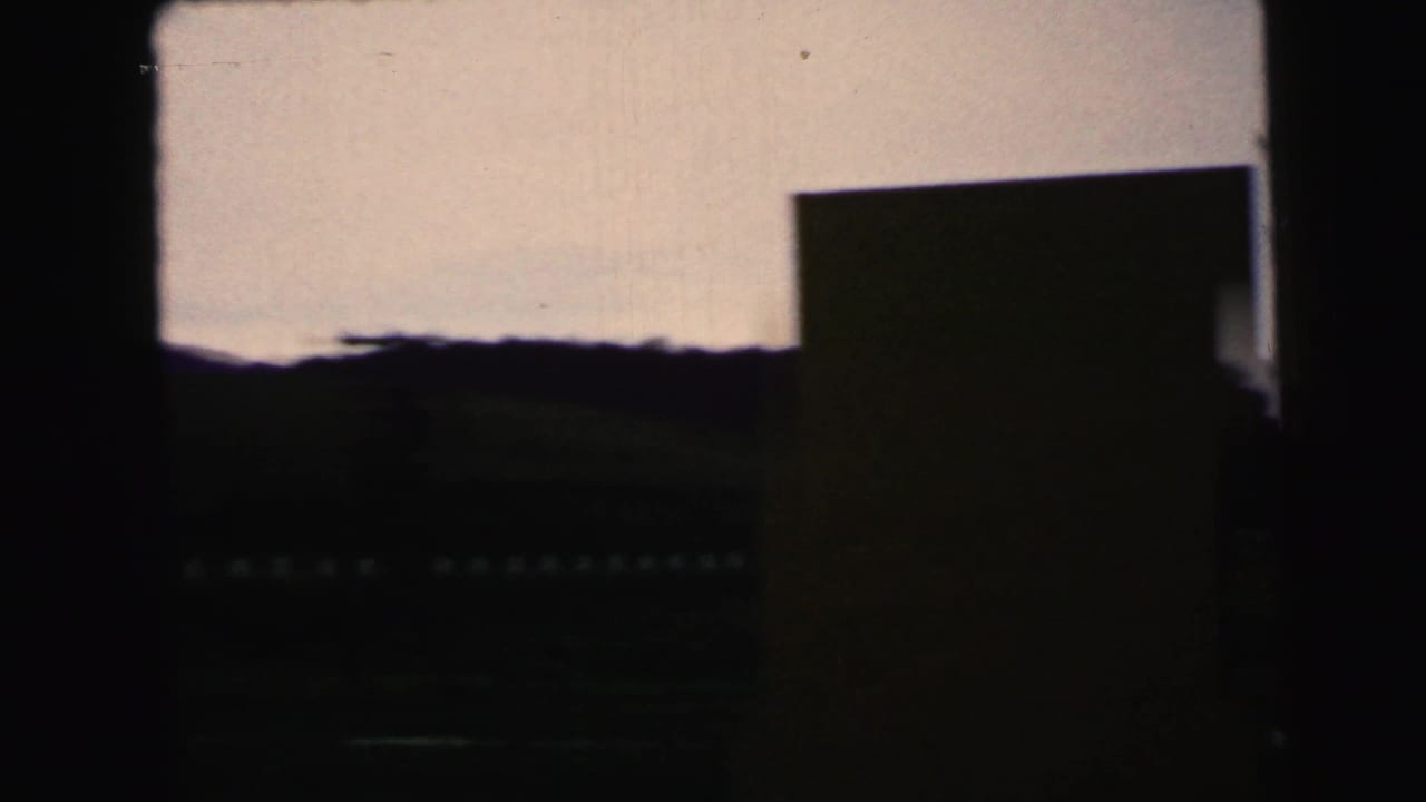 1964 8mm Camden-area view through a dark frame, showing a dim landscape, pale sky, and distant silhouetted trees.