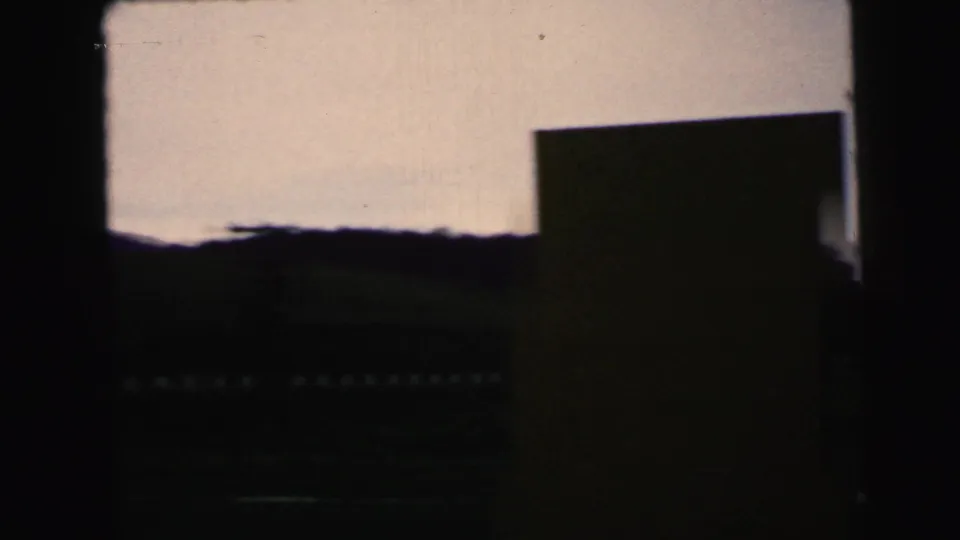 1964 8mm Camden-area view through a dark frame, showing a dim landscape, pale sky, and distant silhouetted trees.