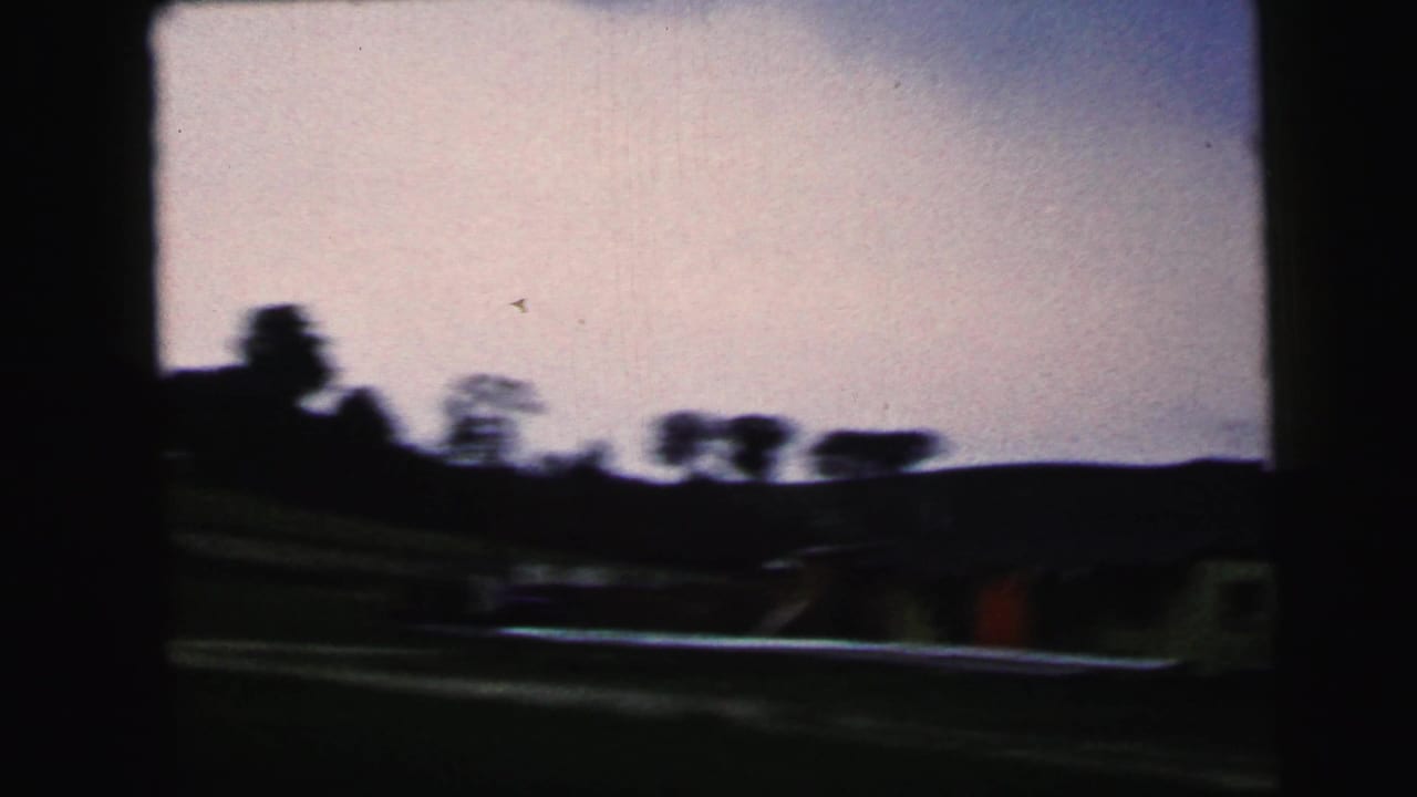 A 1964 Camden-area moving view shows tracks or roadside lines, low ground, and silhouetted trees beneath a pale sky.