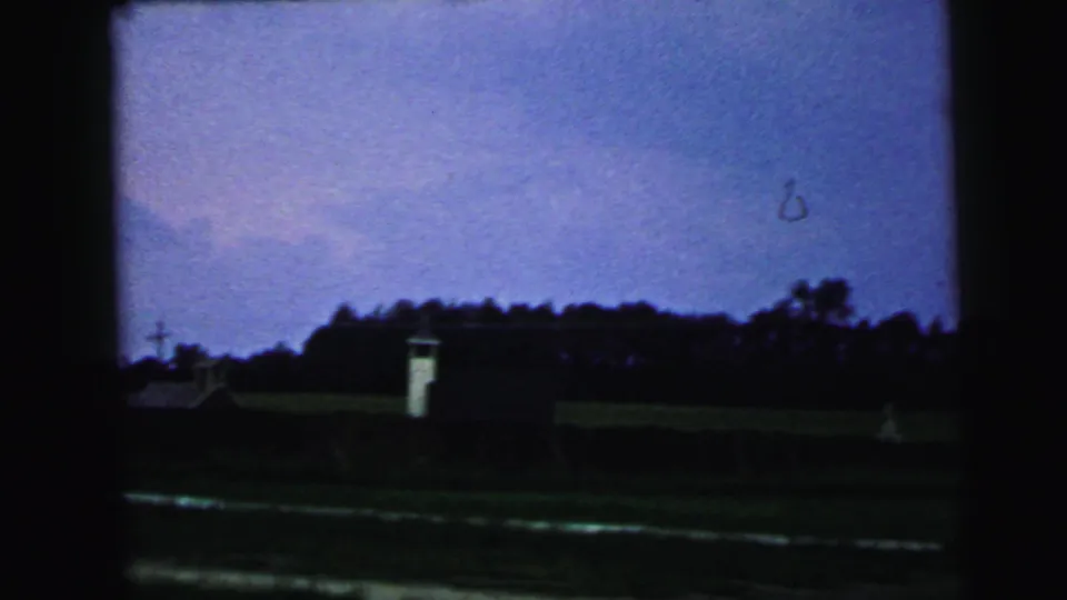 A 1964 Camden-area rail-side view shows a small white structure, open ground, tracks, and a dark tree line under a blue sky.