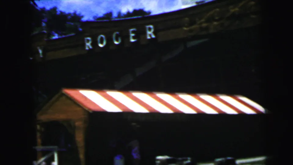 Close view of the waterfront building with partial Roger lettering, a red-and-white striped awning, and deck railing in 1964 Camden footage.