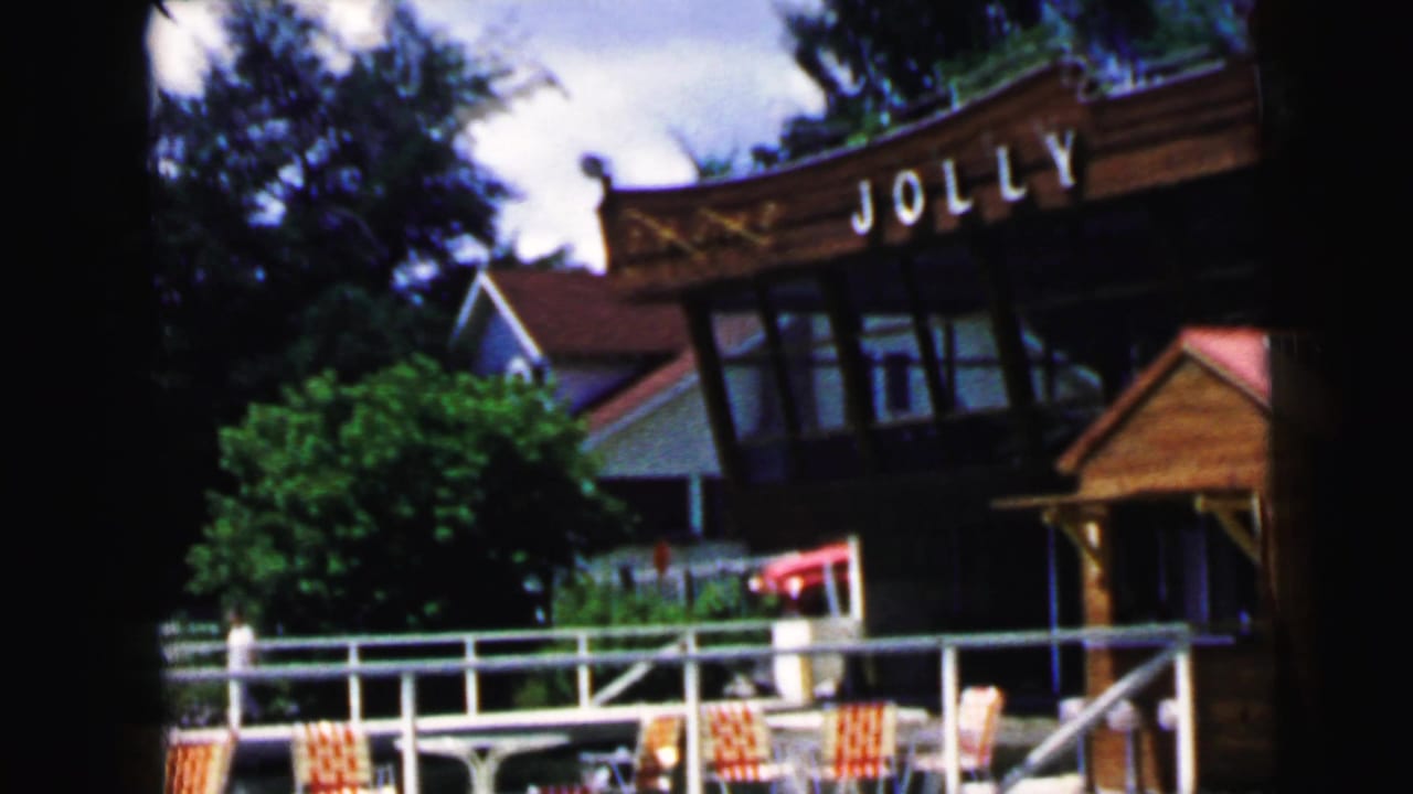 Wooden amusement park entrance with Jolly Roger lettering, railing, chairs and trees.