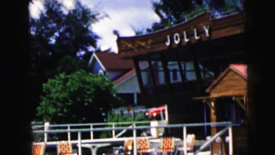 1964 8mm view of the Jolly Roger entrance area in Camden, New Jersey, with wooden facade, railing, chairs and trees.