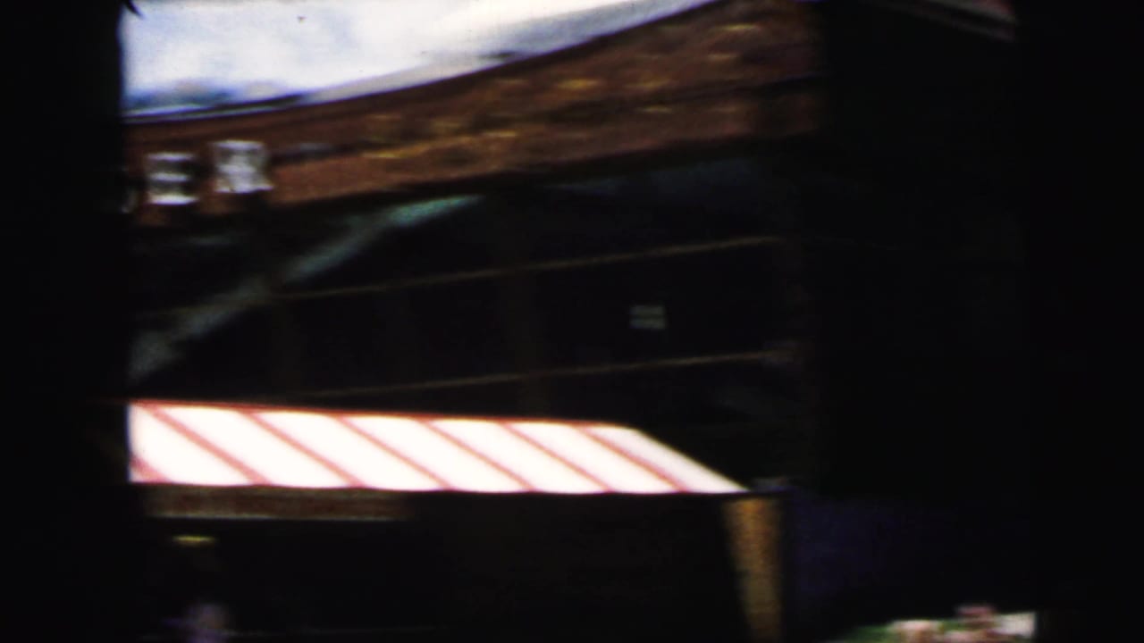 Dark handheld frame of the Camden amusement park entrance, showing a red-and-white striped awning and wooden structure.