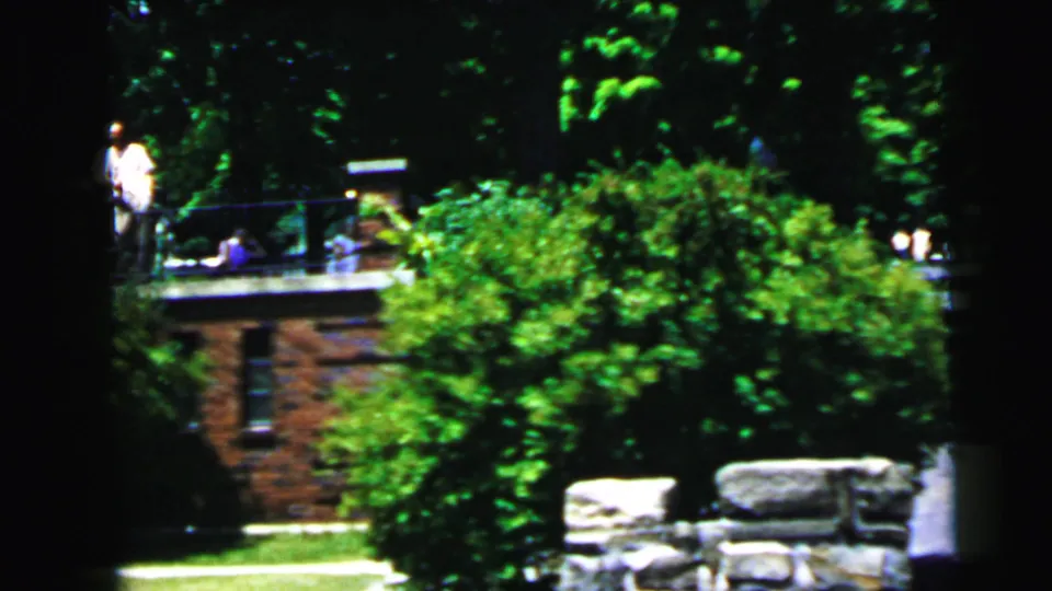 1964 8mm view across Jolly Roger grounds with shrubs, railing, stonework and visitors near the upper walkway.