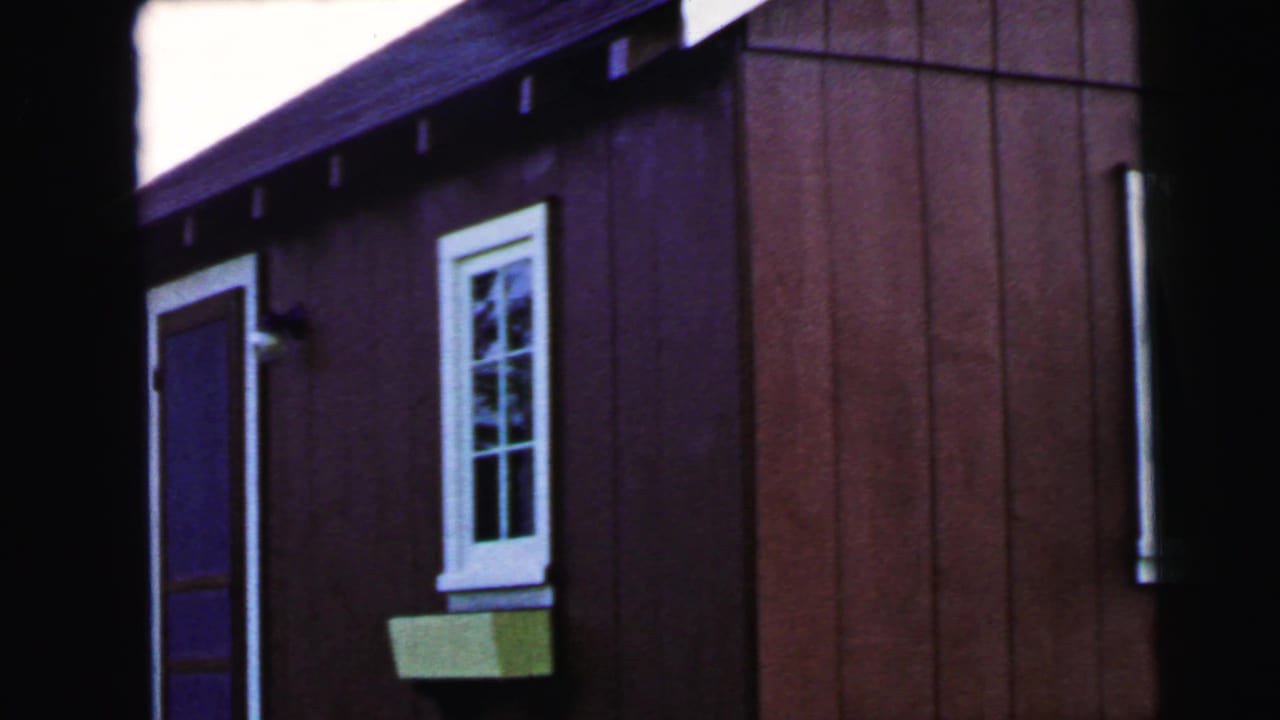 Red wood-sided house exterior with a door, white-trimmed window, and green planter box.