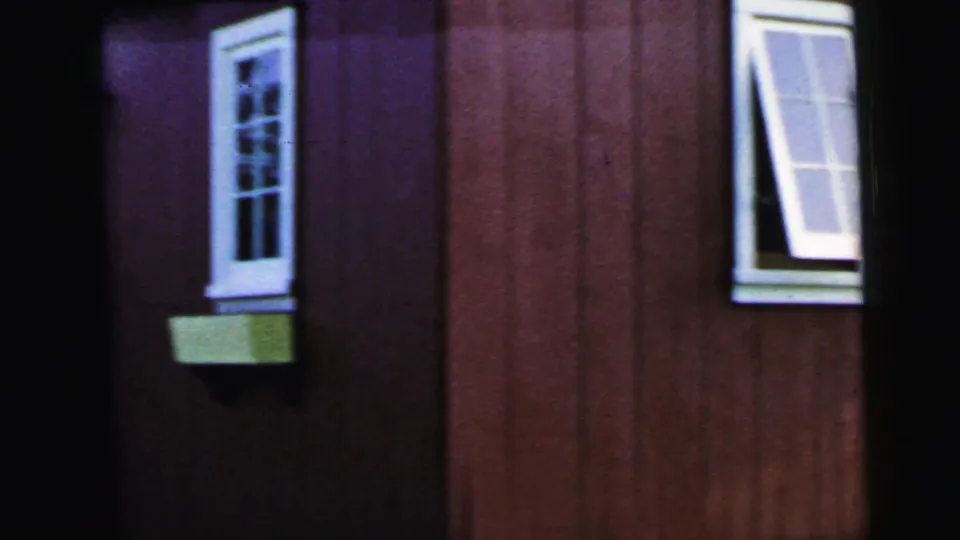 1964 Camden frame showing red vertical siding, a white-trimmed window with planter box, and the edge of an open window nearby.