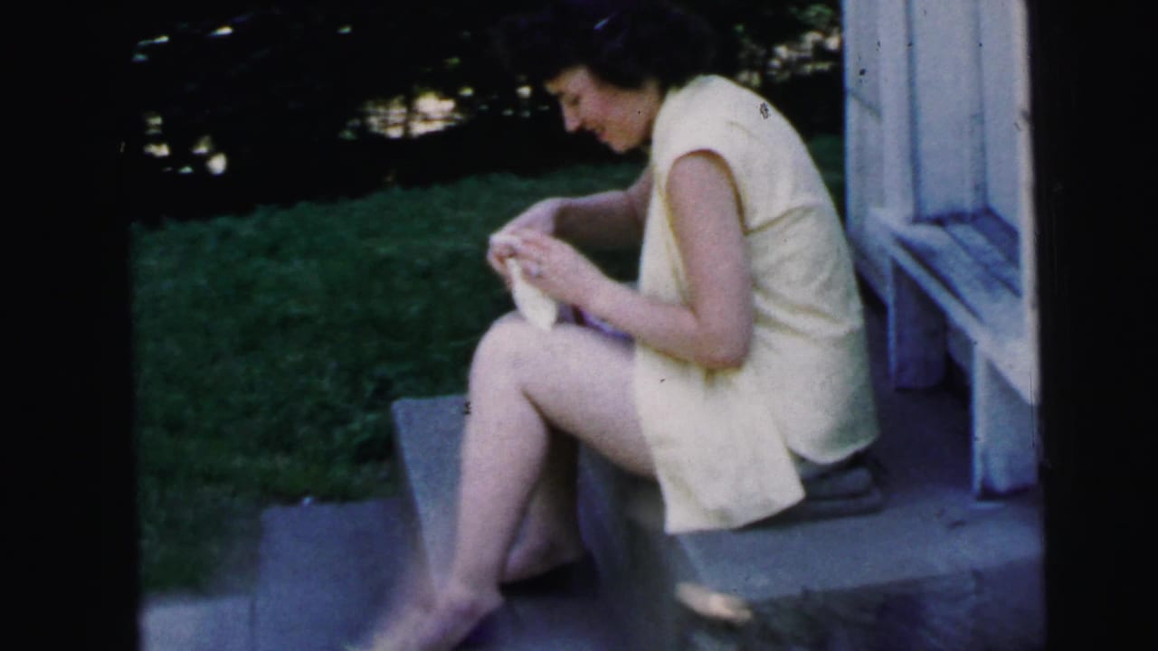Woman in a pale sleeveless dress sits on stone steps writing in a small notebook.