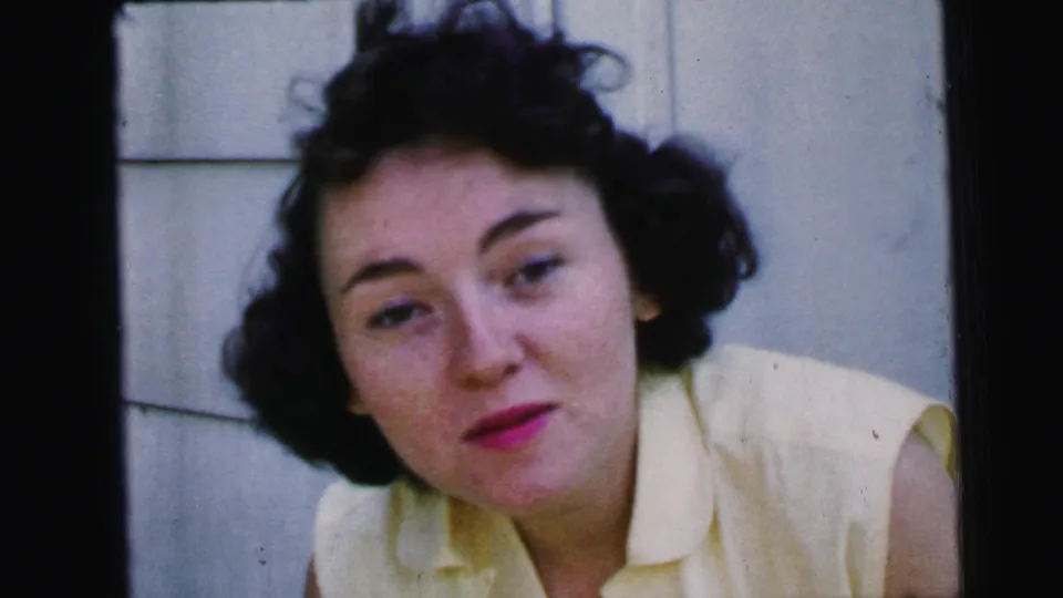 The woman sits near exterior siding in Camden, New Jersey, her expression quieter as the 1964 home-movie camera holds close.