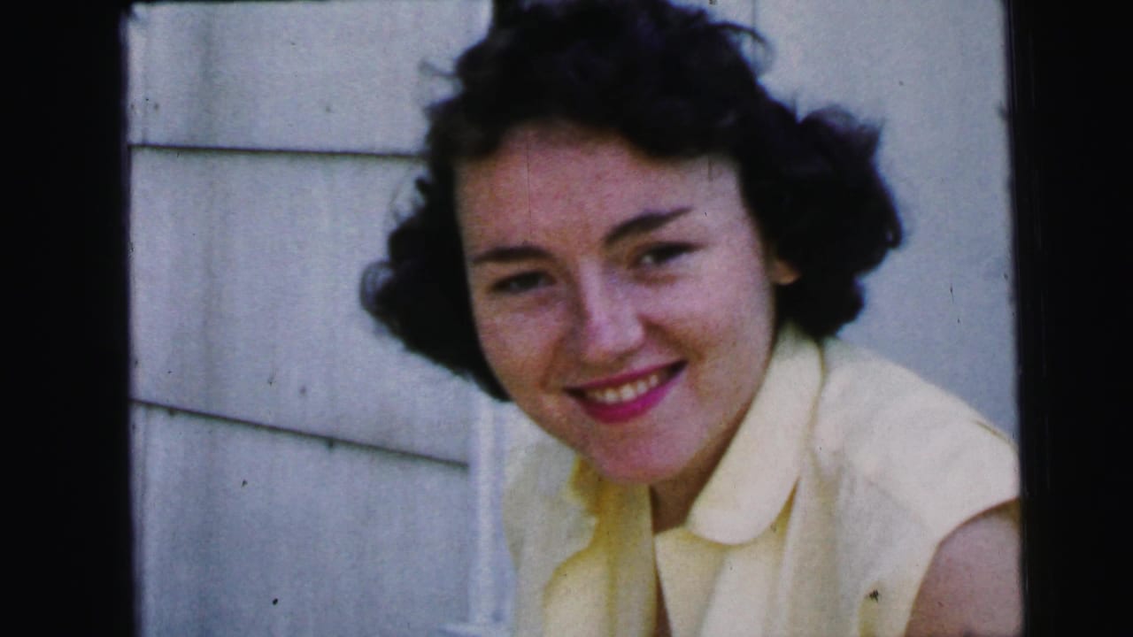 Young woman faces the camera and smiles in front of white siding.