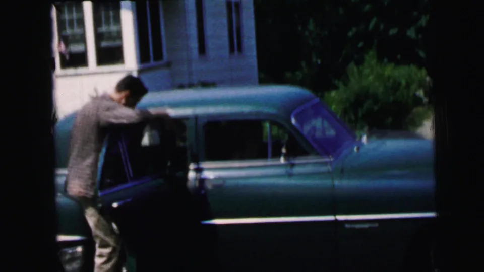 In Camden, New Jersey, 1964 footage, a man in a patterned shirt opens the door of a teal sedan outside a residential house.