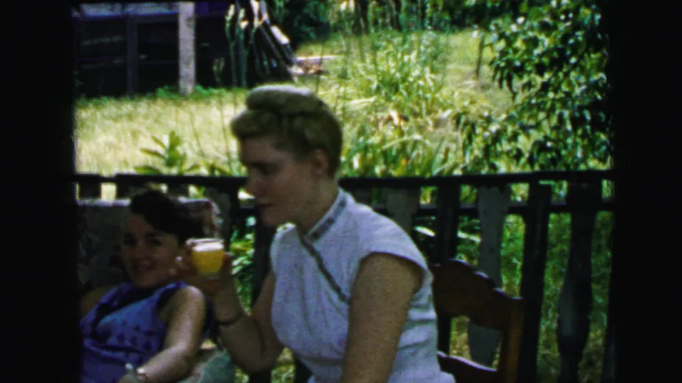 A profile view shows two women on a Camden porch, one in white and one in blue, framed by railing and a green yard beyond.
