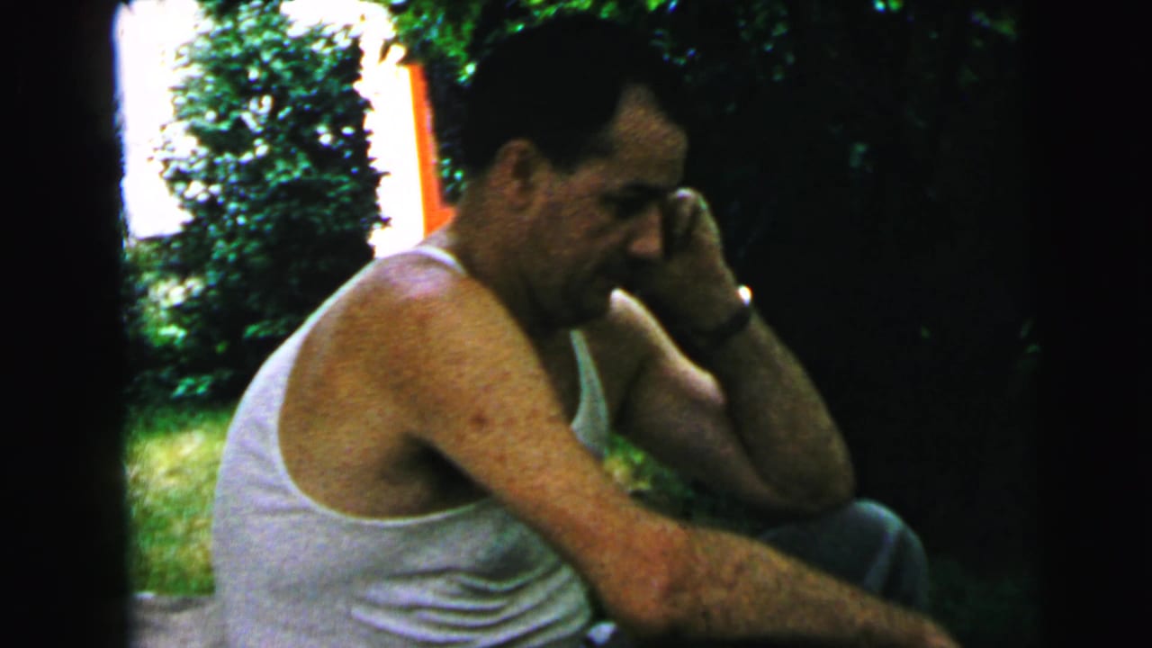 The seated man appears in profile on the steps, with a lawn and shrubs visible in the 1964 Camden setting.