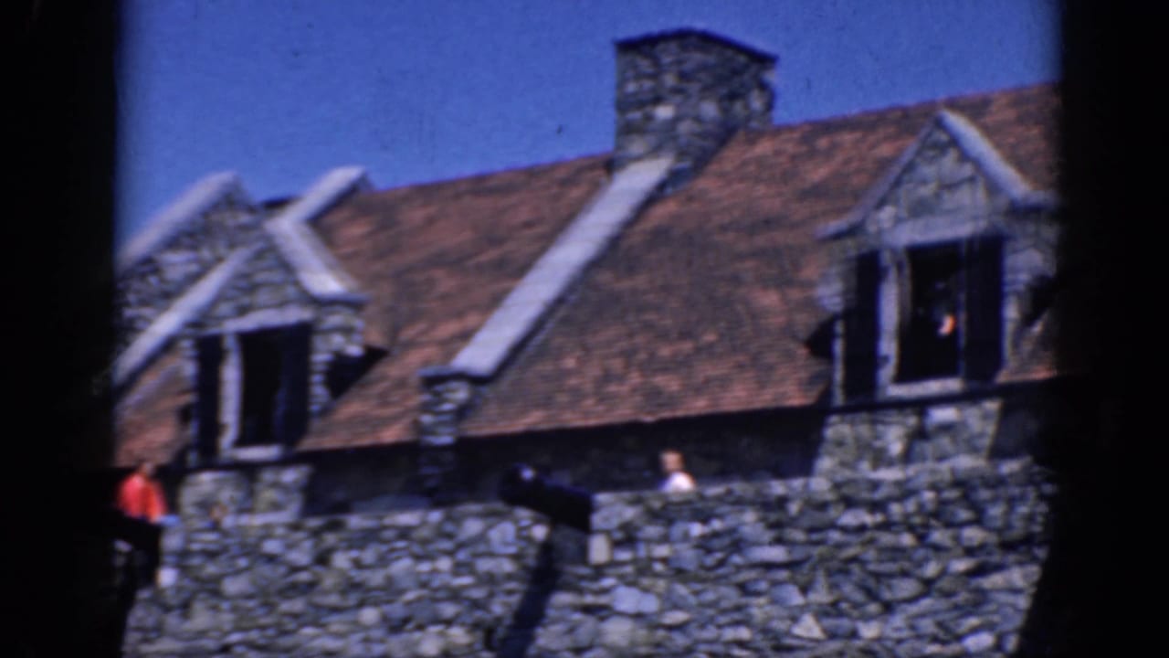 Stone building roofline with people along a parapet and open dormer windows.