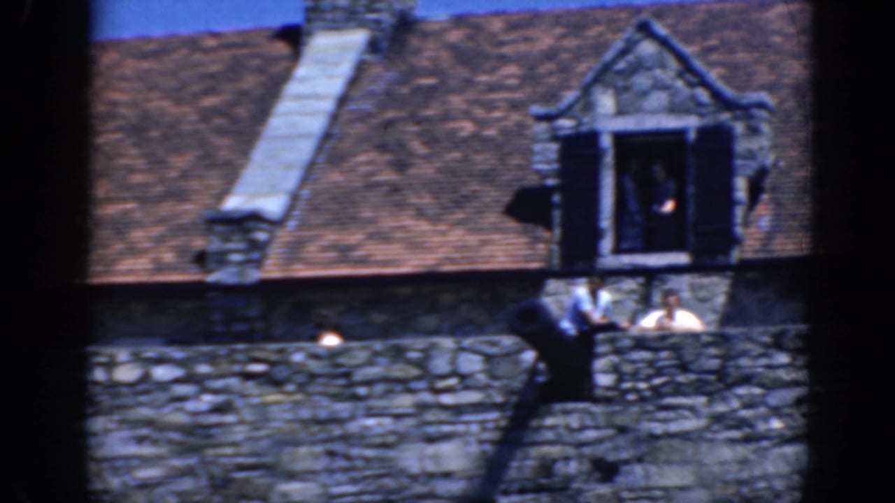 Stone building roof with dormer window, cannon, wall, and visitors on the rampart.