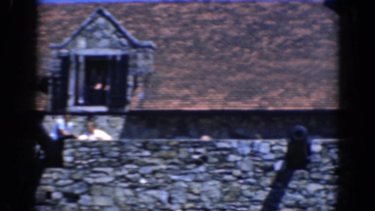 Stone roofline with dormer, cannon, and several distant visitors along the wall.