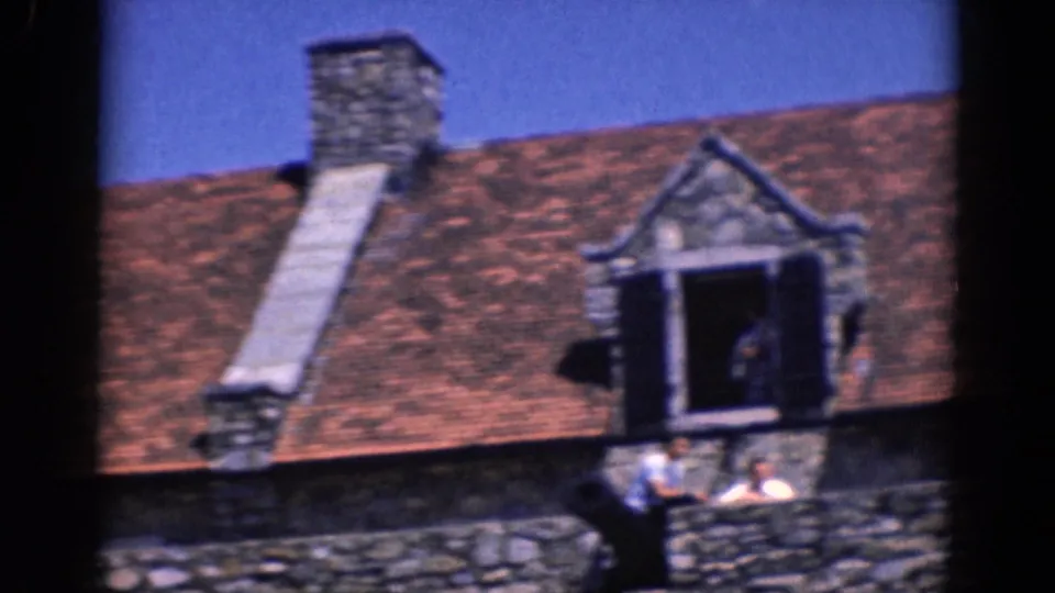 1964 Charlestown, North Carolina home-movie frame with dormer, chimney, stone wall, and distant people near the building.