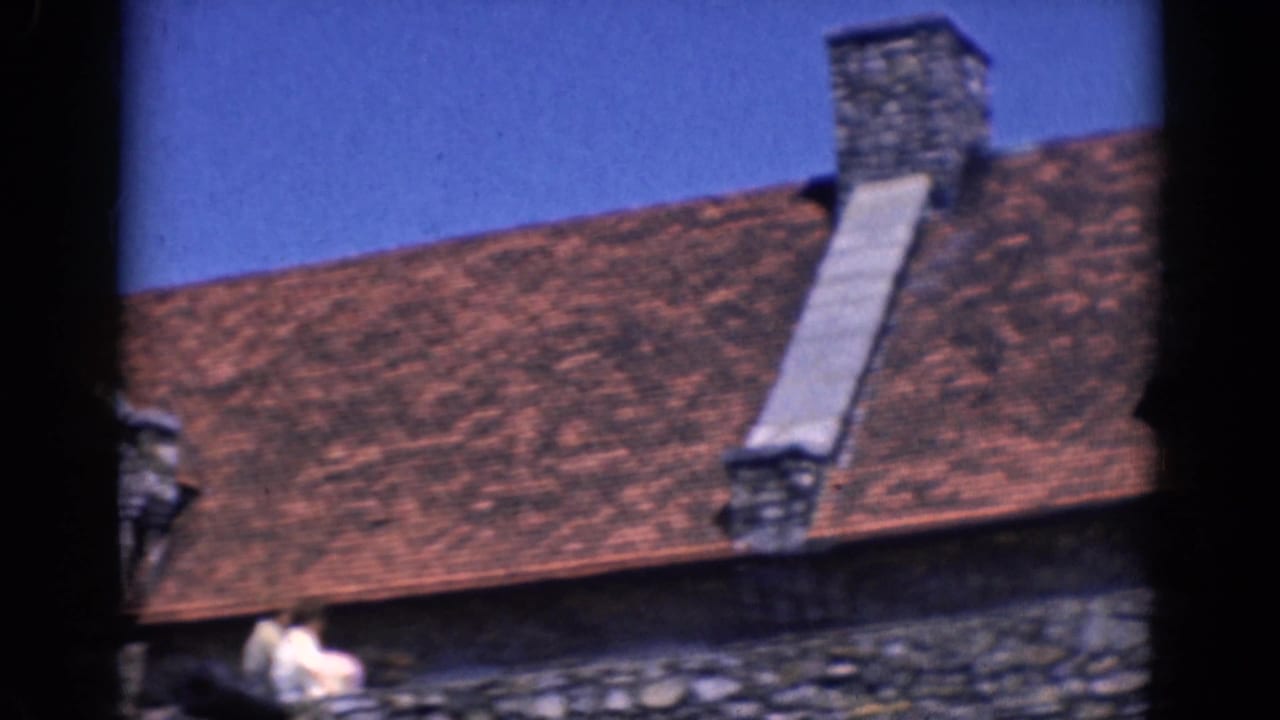 1964 8mm frame of a stone and brick building in Charlestown, North Carolina, showing a red-tiled roof and chimney.