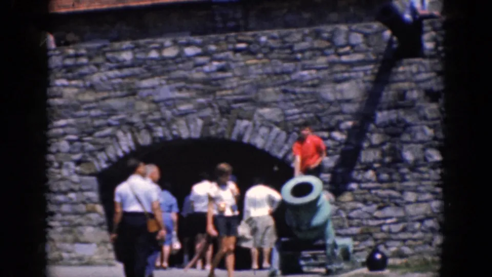 Tourists in 1960s summer clothing gather near a cannon and arched stone entrance at the Charlestown fortress.