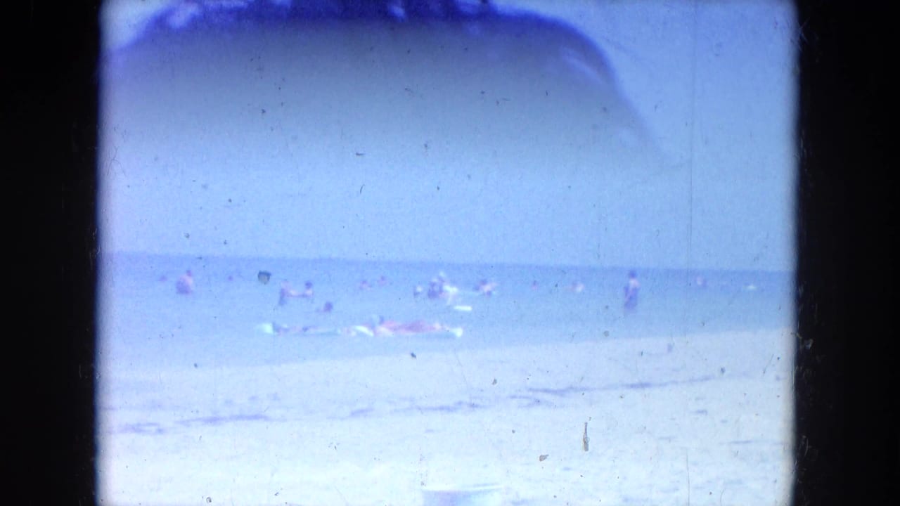 Distant swimmers and beachgoers in shallow surf seen through a dark 8mm film border.