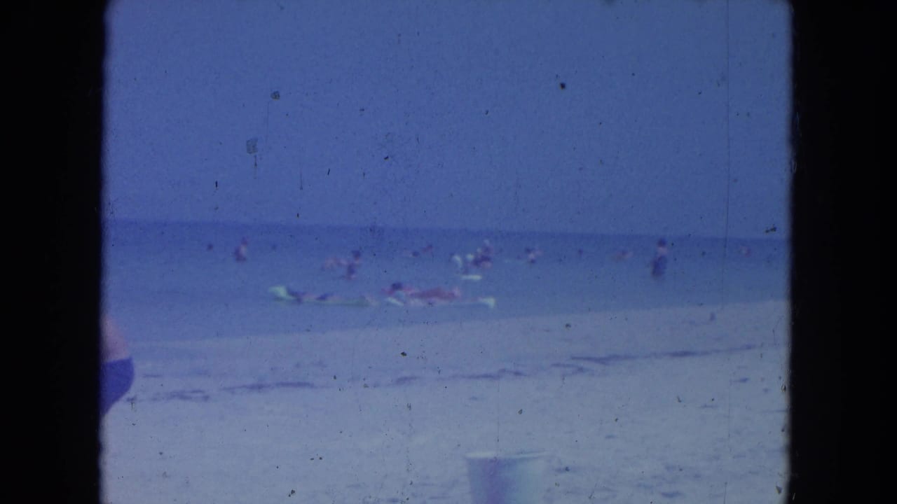 Shoreline with swimmers and beach floats, partially obscured by a vertical dark film border.