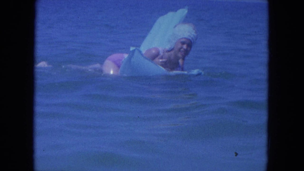 Woman in a swim cap rests on an inflatable ring while a man is partly visible behind her.