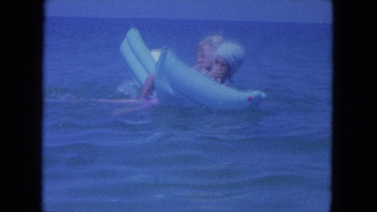 A couple appears side-on in the 1964 Clearwater ocean scene, balancing together on a pale blue inflatable ring.