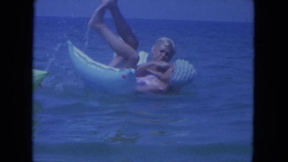 The woman reclines playfully on the light blue ring in Clearwater ocean water, with one leg lifted and small splashes beside the float.