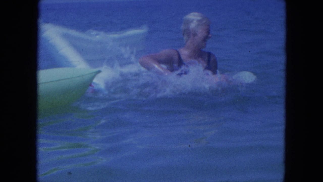 1964 Clearwater home-movie frame showing a woman in a swim cap splashing near a green inflatable float in blue water.