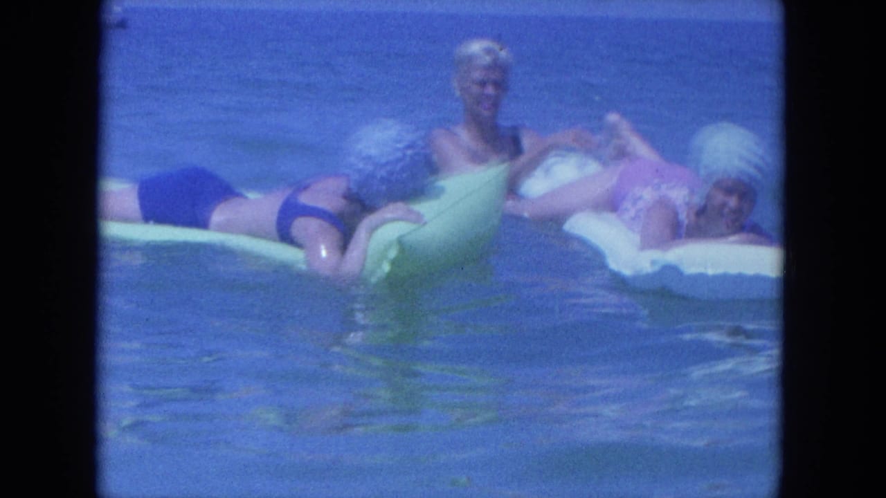 1964 Clearwater footage frame with three women on inflatable floats in blue water, including one seated upright and smiling.
