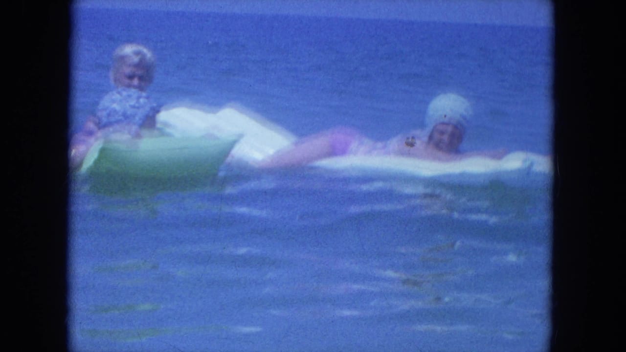 Three women in 1964 Clearwater beach footage float on green and white inflatables in calm blue ocean water.