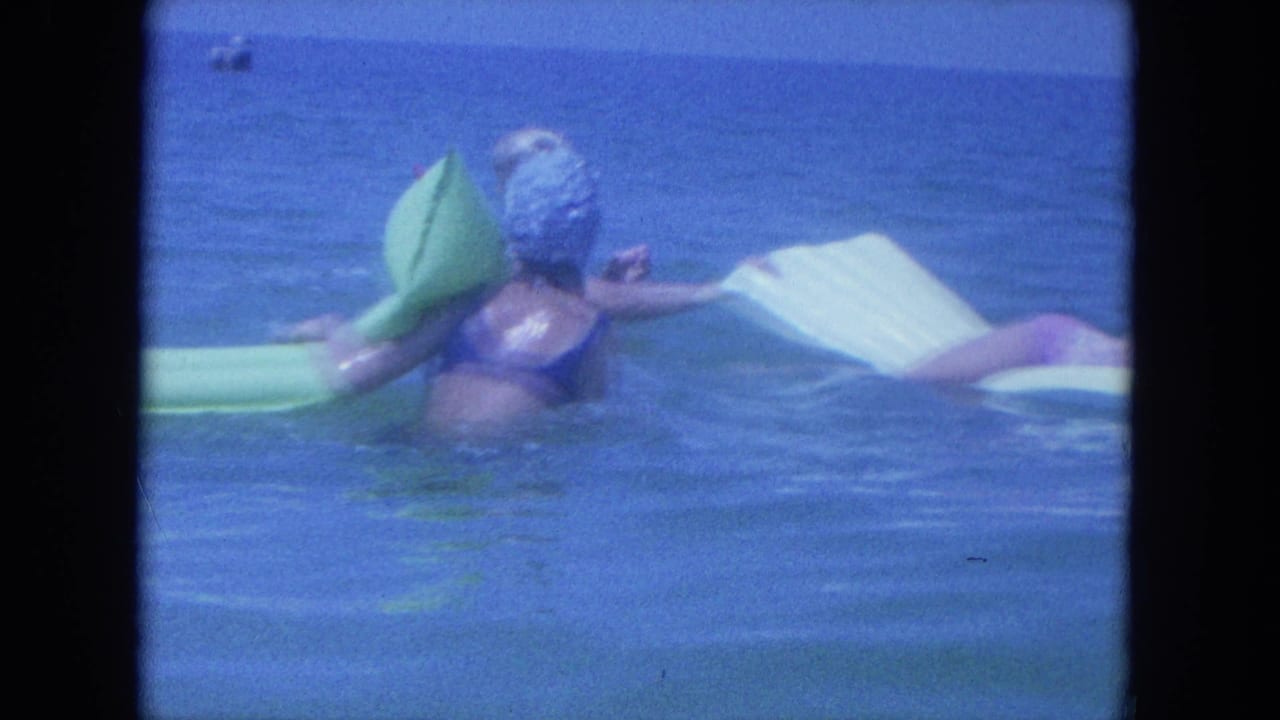 A woman in a blue swim cap floats in calm Clearwater water beside green and white inflatable rafts.