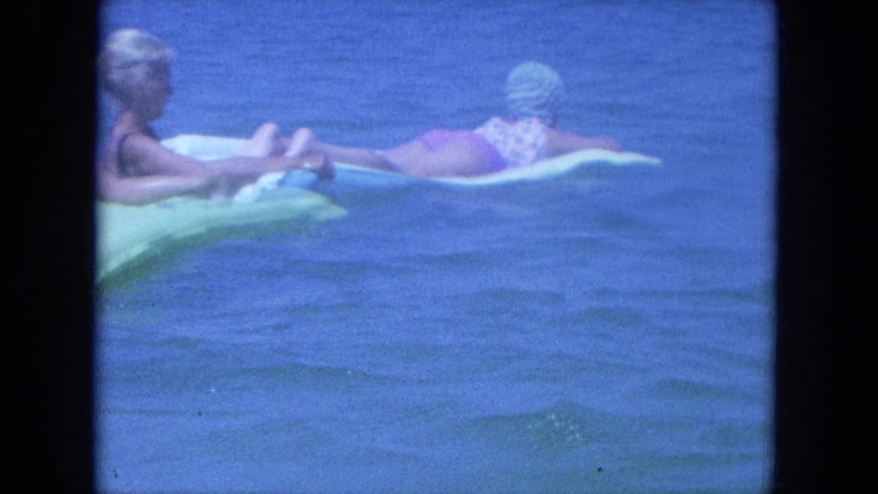 In the Clearwater home-movie shot, one woman reclines on an inflatable mat while another remains beside her in the water.